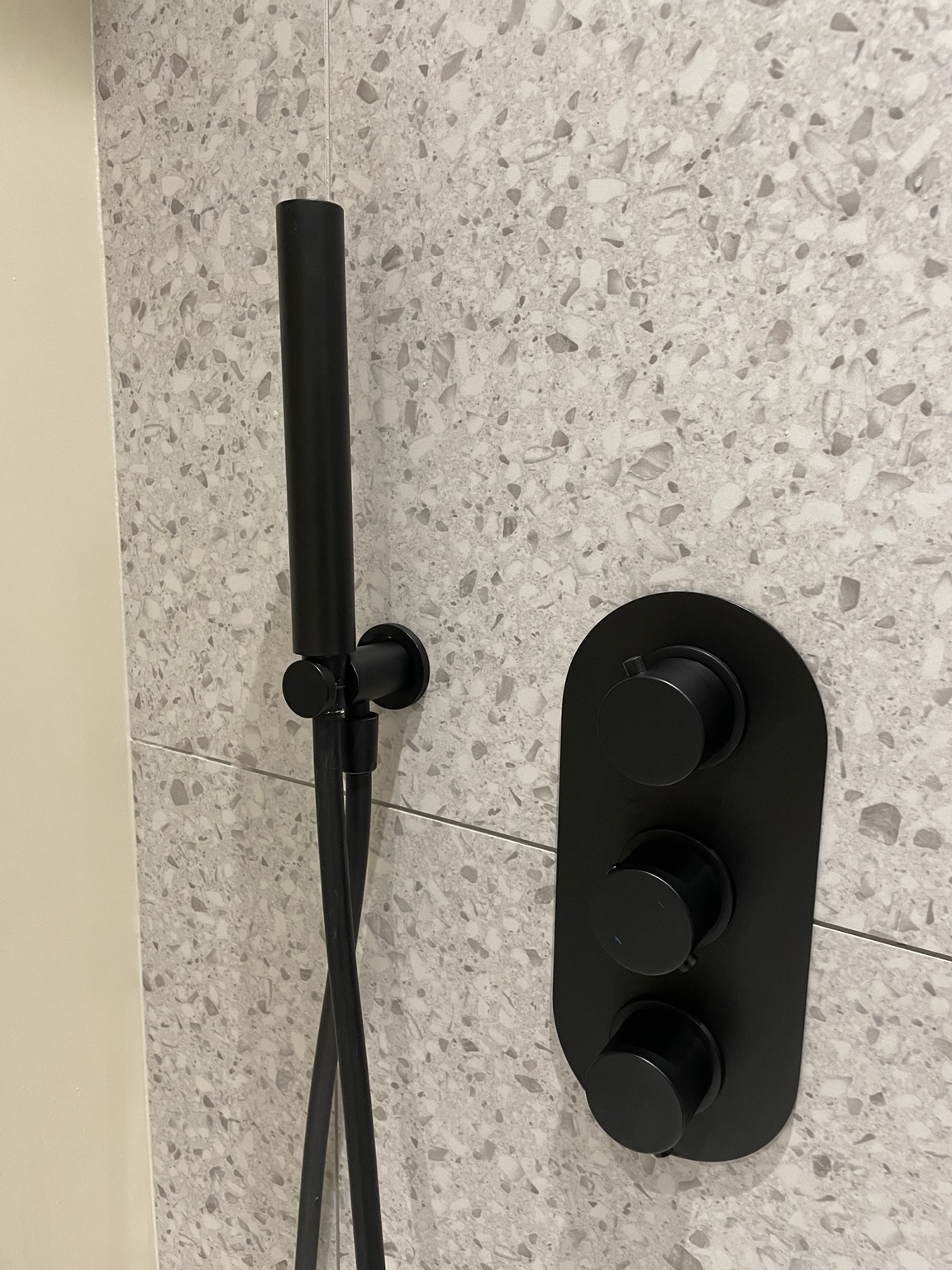 Black shower fittings and clean stone tiles in a bathroom cared for by Sylvia.